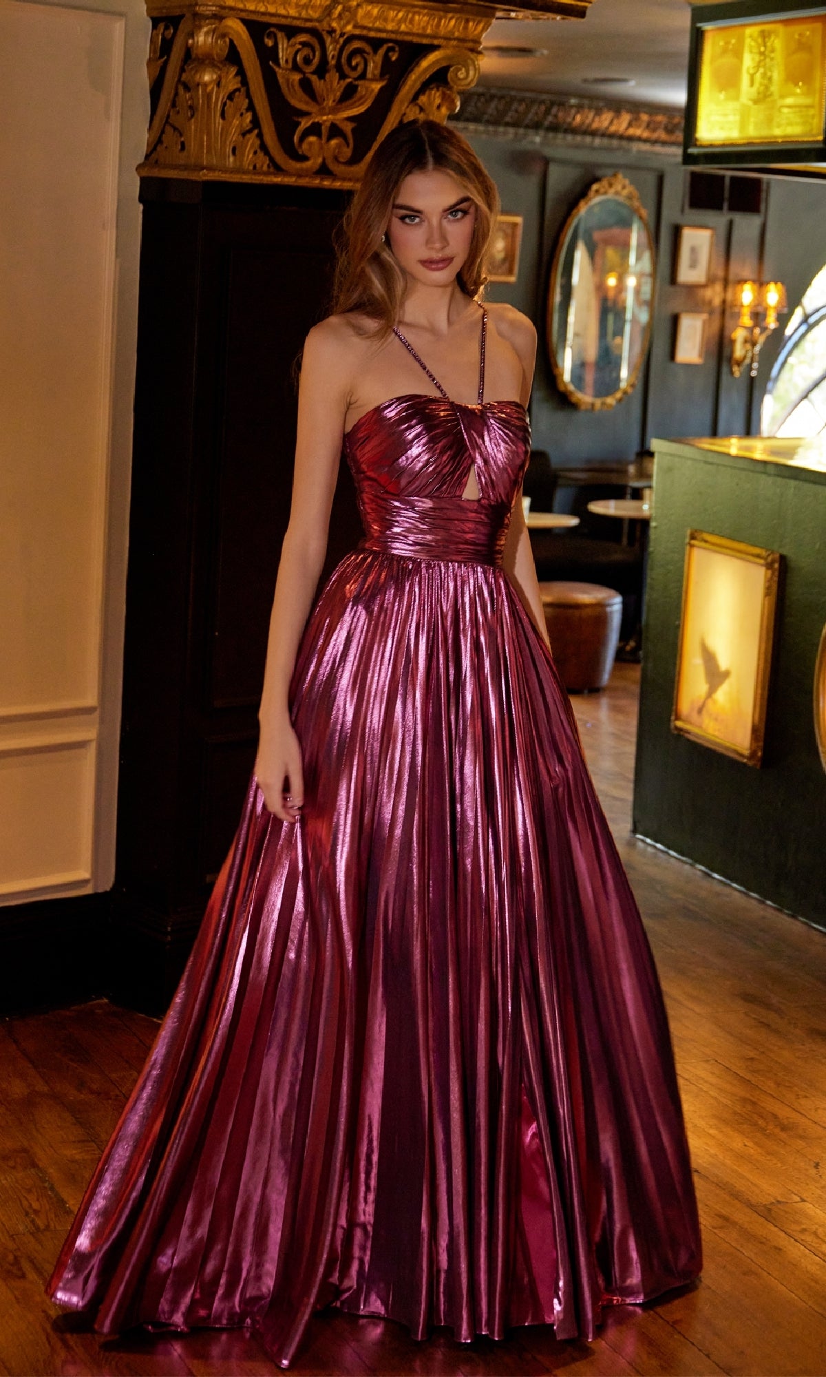 A woman stands indoors wearing the Juliet JT2503A, a long metallic magenta A-line prom dress featuring a strapless neckline, pleated skirt, and subtle strappy-back detail.